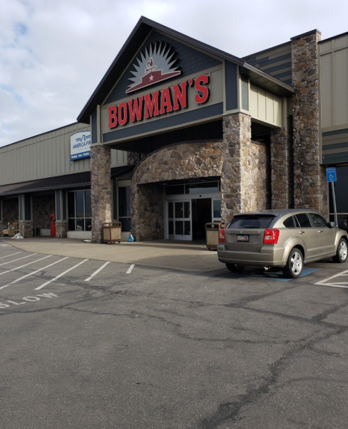 Exterior of Bowman's store featuring a stone facade and a parked car in front. Cloudy sky above.