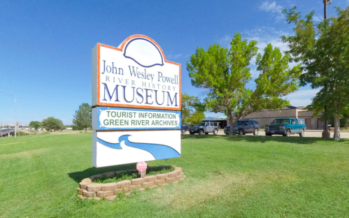 Sign for the John Wesley Powell River History Museum, with green grass and blue sky in the background.