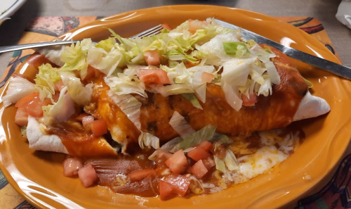 A plate of enchiladas topped with lettuce, diced tomatoes, and red sauce, served on an orange dish.