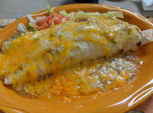 A large burrito topped with melted cheese, served on a plate with lettuce and tomato.