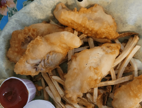 A basket of golden fried fish fillets served with crispy French fries and dipping sauces.