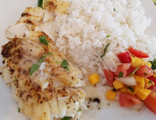 A plate featuring grilled fish with a creamy sauce, served with white rice and a fresh mango-tomato salad.