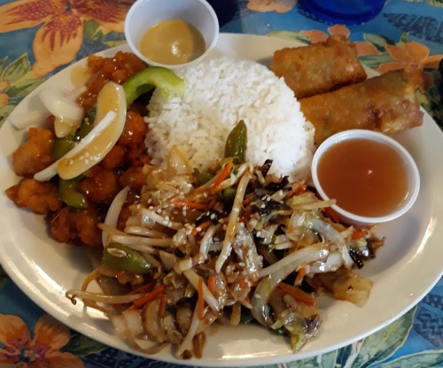 A plate of Chinese food featuring rice, sweet and sour chicken, spring rolls, and a vegetable stir-fry with sauce.