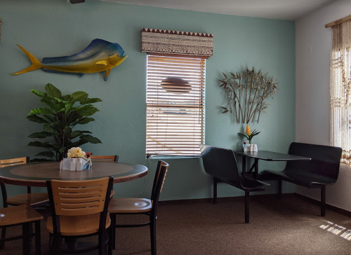 Cozy dining area with a round table, black seating, and tropical decor, including a fish and plants by the window.