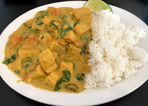 A plate of creamy curry with tofu and spinach, served with a side of fluffy white rice and a lime wedge.