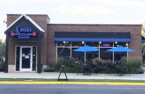 Exterior of Kainoa's Hawaiian Grill, featuring blue umbrellas, an "Open" sign, and a welcoming atmosphere.