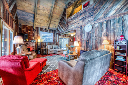 Cozy cabin interior with wooden walls, a high ceiling, red and gray sofas, and warm lighting.