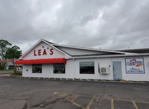 Exterior of Lea's restaurant with a red awning, cloudy sky, and parking lot in front.