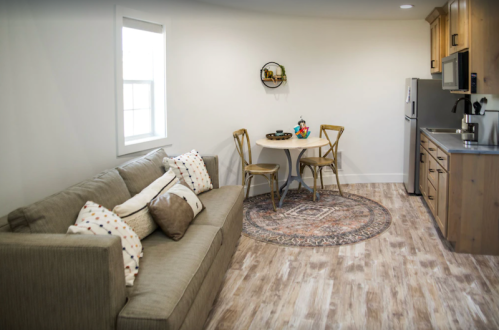 Cozy living space featuring a sofa, dining table with two chairs, and a kitchen area with wooden cabinets.