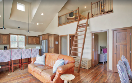 Cozy interior of a modern cabin featuring a living area, kitchen, and a loft accessed by a wooden ladder.