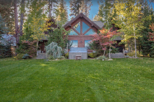 A large log cabin surrounded by trees and a well-maintained lawn, featuring a spacious front entrance.