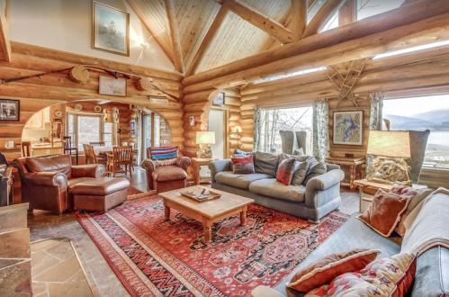Cozy log cabin interior with a spacious living area, wooden beams, plush seating, and a warm rug.