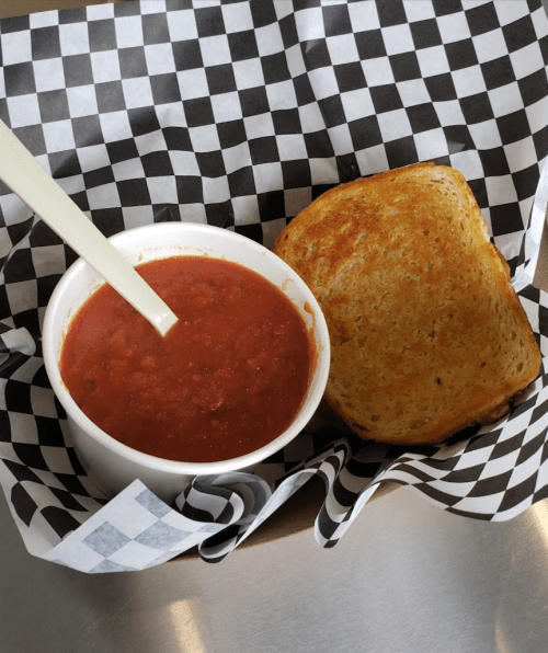 A bowl of tomato soup with a spoon, accompanied by a slice of toasted bread, served in a checkered basket.
