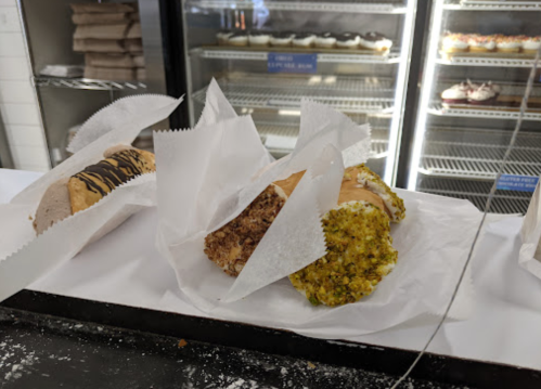 Three pastries on a counter, wrapped in parchment paper, with various toppings and fillings, in a display case background.