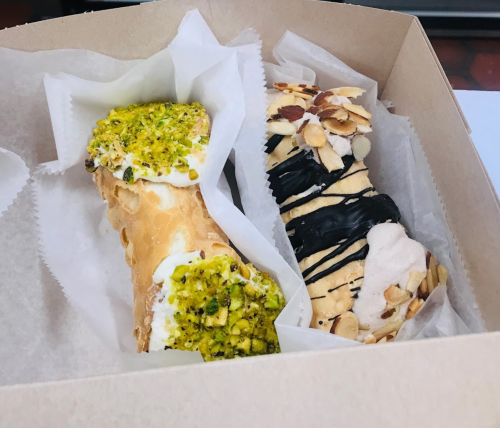 Two delicious cannoli in a box: one topped with pistachios and the other with chocolate and almond flakes.