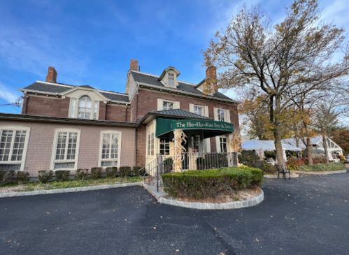 Historic building with a green awning reading "The Ho-Ho-Kus Inn & Tavern," surrounded by trees and a clear blue sky.