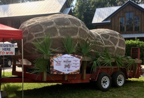 A large, peanut-shaped sculpture on a trailer, displayed at an outdoor event with a registration tent nearby.