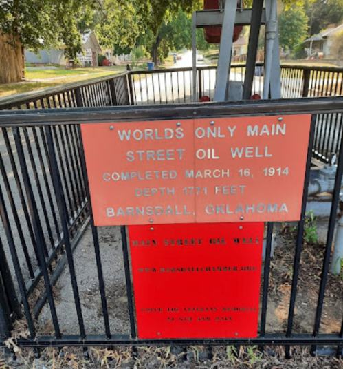 Sign for the "World's Only Main Street Oil Well" in Barnsdall, Oklahoma, detailing its completion date and depth.