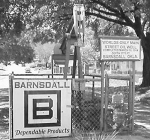 Sign for Barnsdall, Oklahoma, featuring the world's only main street oil well, with a vintage oil pump in the background.