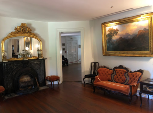 Elegant room featuring a vintage fireplace, ornate mirror, and a plush orange sofa with a large landscape painting.