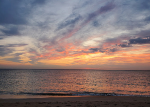 A serene beach at sunset, with colorful clouds reflecting on the calm ocean waters.