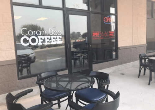 Exterior of Coram Deo Coffee shop with outdoor seating and an "Open" sign in the window.