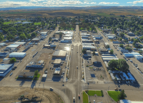 Aerial view of a small town with streets, buildings, and green spaces under a clear blue sky.