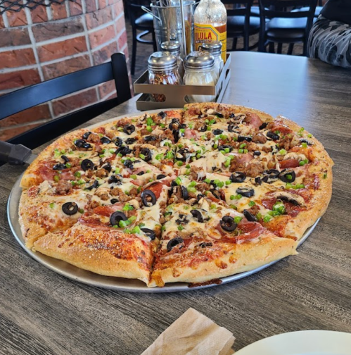 A large pizza topped with pepperoni, sausage, olives, green peppers, and cheese, served on a metal tray.