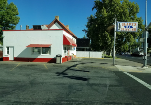 A white building with red accents, featuring a sign for "Glade's Drive-Inn," located at a street intersection.