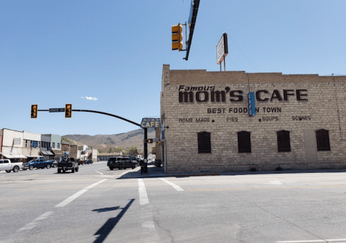 A street view of Mom's Cafe, featuring a sign that reads "Best Food in Town" and nearby traffic signals.