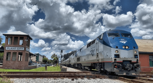 Amtrak train passing by the Plant City station under a cloudy sky.
