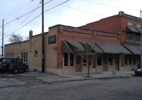 A brick building with a sign reading "Dali's," featuring awnings and a parked vehicle nearby.