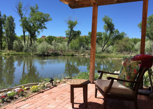 A serene view of a river surrounded by greenery, seen from a porch with a chair and small table.