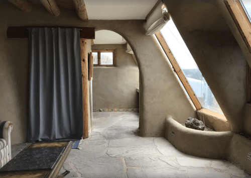 A cozy, modern interior with curved walls, large windows, and natural materials, featuring a stone floor and wooden accents.