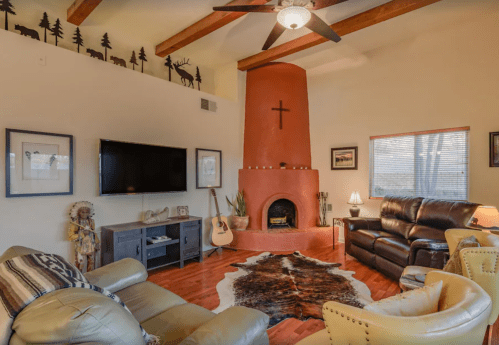 Cozy living room with a red fireplace, wooden beams, leather furniture, and a guitar, featuring rustic decor.