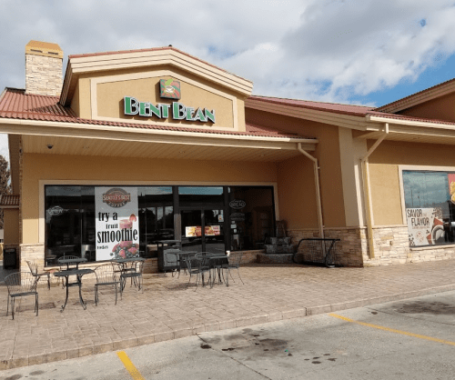 Exterior of a café named "Bent Bean," featuring outdoor seating and large windows with promotional signage.
