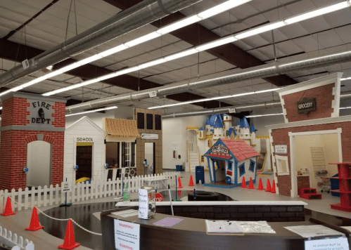 A colorful indoor play area featuring miniature buildings like a fire department, school, and grocery store.