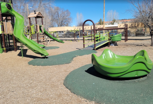 A playground featuring green slides, a climbing structure, and a spinning seat on a rubber surface.