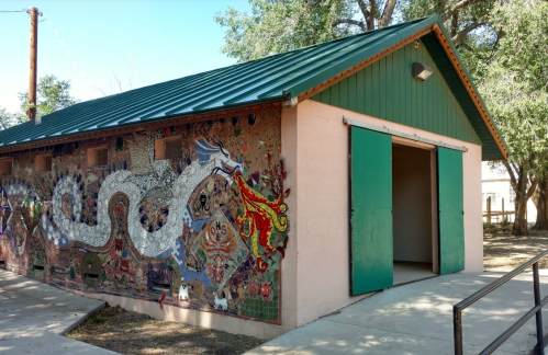 A colorful mural of a dragon and other designs on a building with green doors and a metal roof.