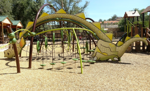 A colorful dragon-themed playground structure with climbing features and swings, set in a sunny outdoor area.
