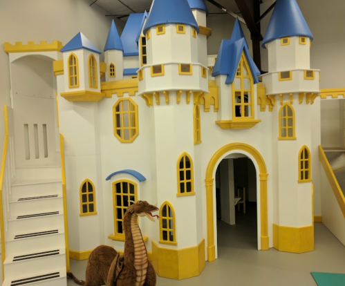 A colorful play castle with blue roofs and yellow accents, featuring a staircase and a toy dragon nearby.