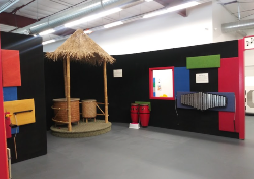 A colorful play area featuring musical instruments, a thatched roof structure, and vibrant wall panels.