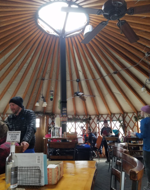Interior of a round, wooden restaurant with a high ceiling, featuring a skylight and patrons enjoying their meals.