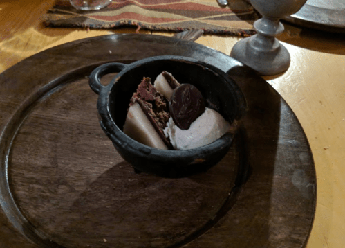 A small black bowl on a wooden plate containing chocolate dessert and a scoop of ice cream.