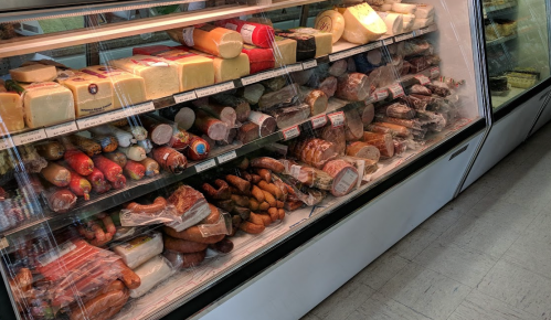 A display case filled with various meats, cheeses, and packaged deli items, all neatly arranged and wrapped.