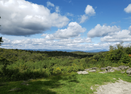 A scenic view of rolling hills and a cloudy sky, with lush greenery and rocky foreground.