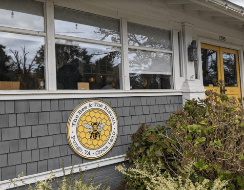 Exterior of The Bee & The Biscuits restaurant in Pungo, VA, featuring a sign with a bee and honeycomb design.