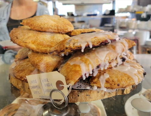 A stack of glazed pastries with a variety of fillings, displayed on a wooden platter in a bakery.