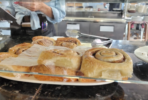 A display of freshly baked cinnamon rolls on a plate, covered with parchment paper, in a café setting.