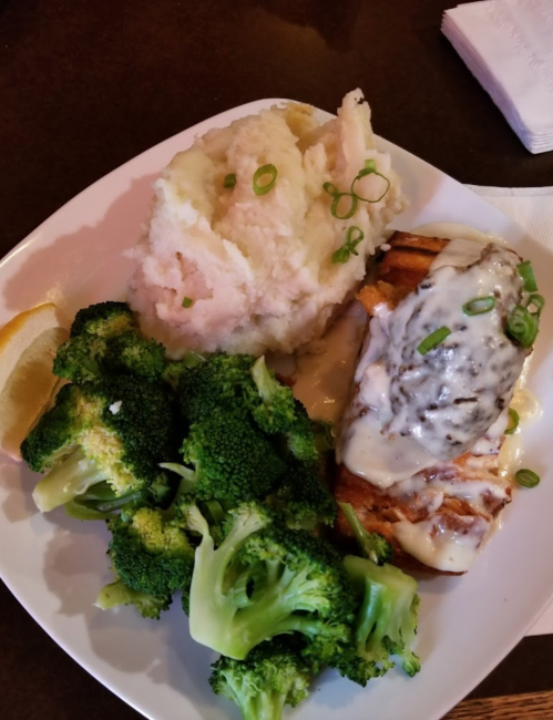 A plate with grilled salmon topped with sauce, mashed potatoes, and steamed broccoli, garnished with green onions.